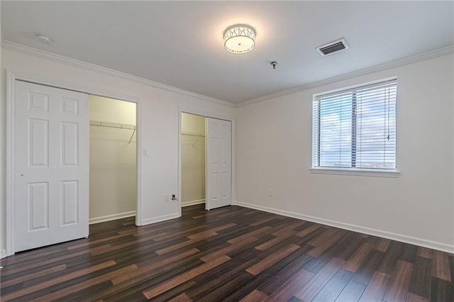 unfurnished bedroom featuring dark hardwood / wood-style floors, ornamental molding, and multiple closets