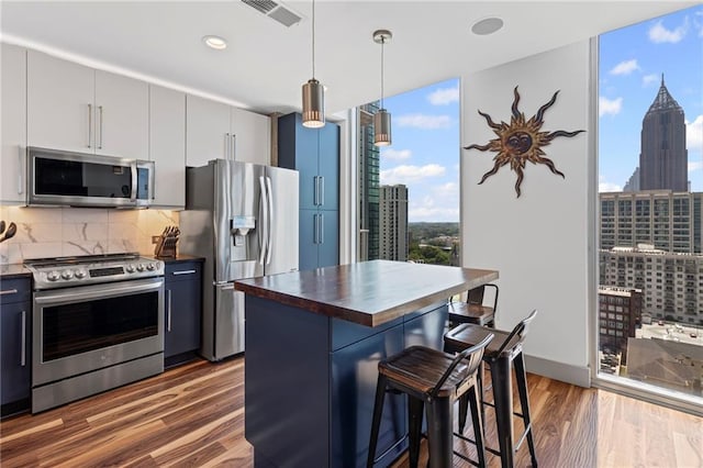 kitchen with appliances with stainless steel finishes, wooden counters, a wall of windows, a kitchen bar, and tasteful backsplash