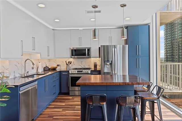 kitchen featuring appliances with stainless steel finishes, a sink, blue cabinets, butcher block countertops, and recessed lighting