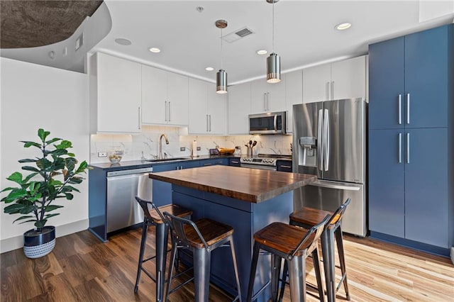 kitchen with appliances with stainless steel finishes, wooden counters, blue cabinets, a kitchen bar, and light wood finished floors