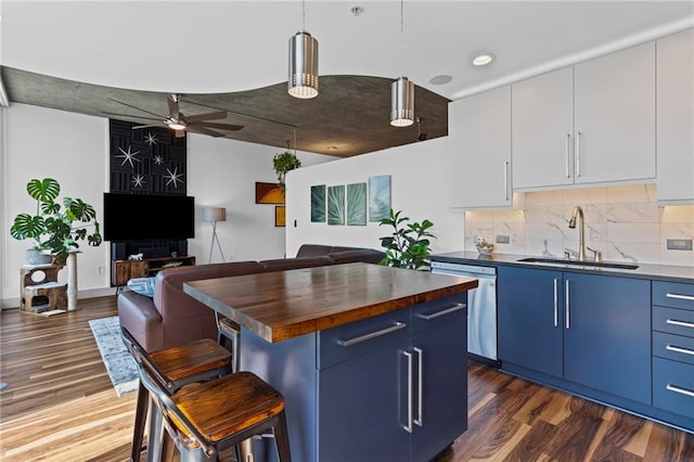 kitchen featuring blue cabinetry, a sink, stainless steel dishwasher, butcher block countertops, and open floor plan