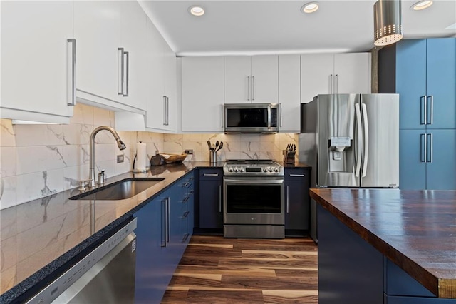 kitchen with appliances with stainless steel finishes, a sink, blue cabinets, butcher block countertops, and dark wood finished floors