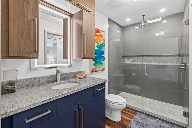 full bath featuring toilet, vanity, a shower stall, wood finished floors, and recessed lighting