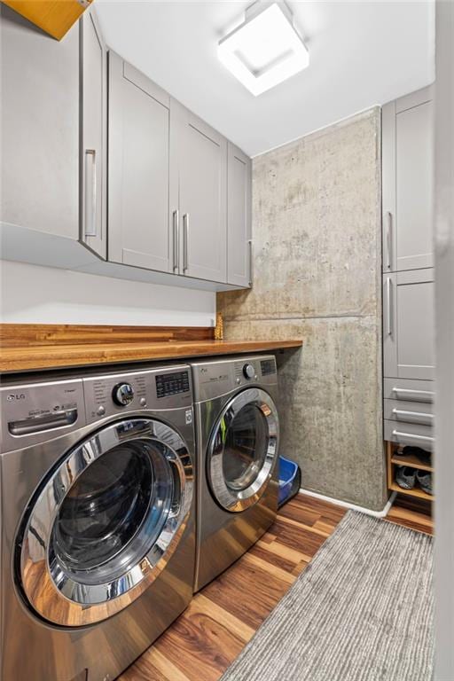 laundry room with washing machine and dryer, wood finished floors, and cabinet space