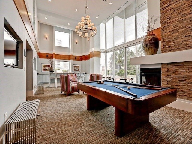 recreation room with a towering ceiling, billiards, a chandelier, carpet flooring, and a multi sided fireplace