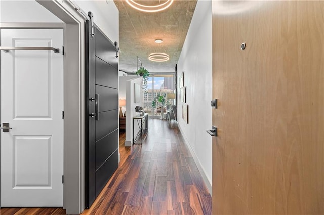 hall with dark wood-type flooring, a barn door, and baseboards