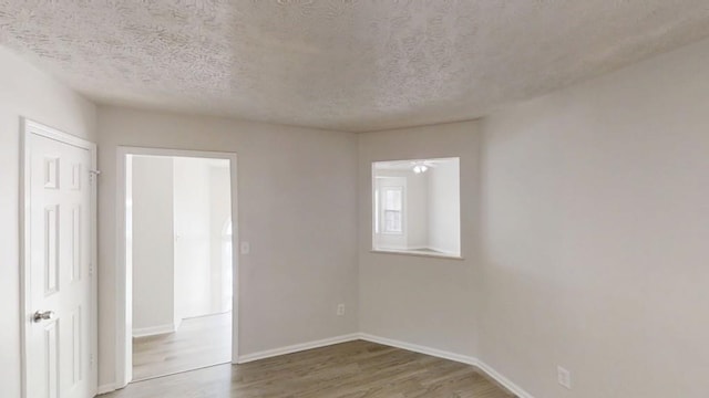 spare room with a textured ceiling, baseboards, and wood finished floors