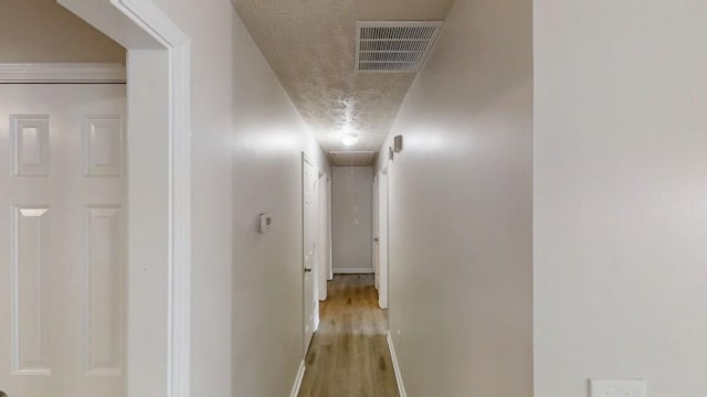 hallway with a textured ceiling, visible vents, baseboards, light wood-type flooring, and attic access