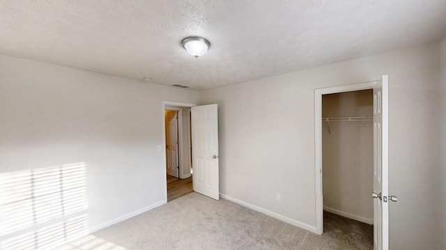 unfurnished bedroom featuring a textured ceiling, light colored carpet, visible vents, baseboards, and a closet