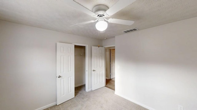 unfurnished bedroom featuring baseboards, visible vents, light colored carpet, a textured ceiling, and a closet