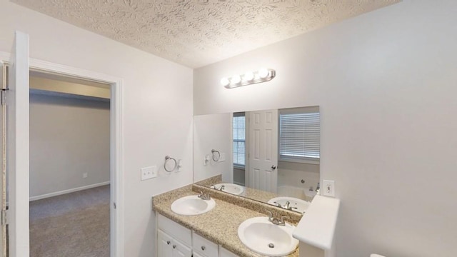 full bath with double vanity, a textured ceiling, baseboards, and a sink