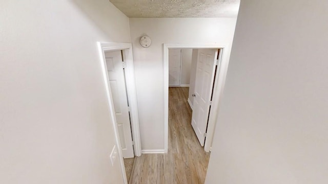 hall featuring light wood finished floors, baseboards, and a textured ceiling