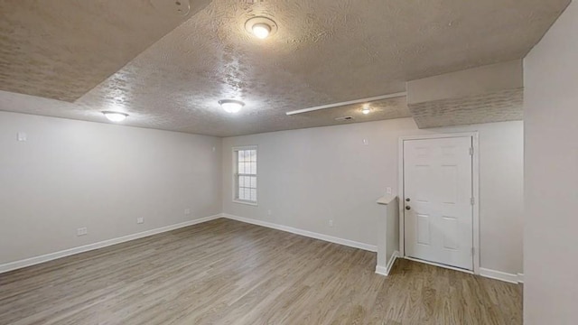 basement featuring a textured ceiling, baseboards, and wood finished floors