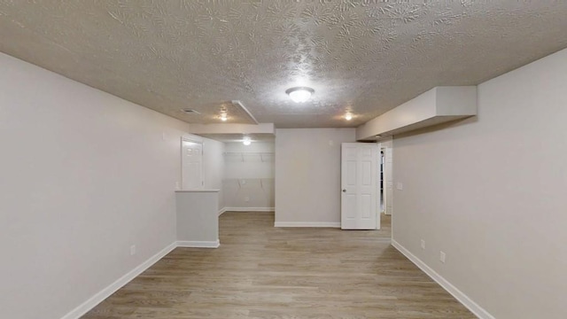 finished below grade area with visible vents, a textured ceiling, baseboards, and wood finished floors