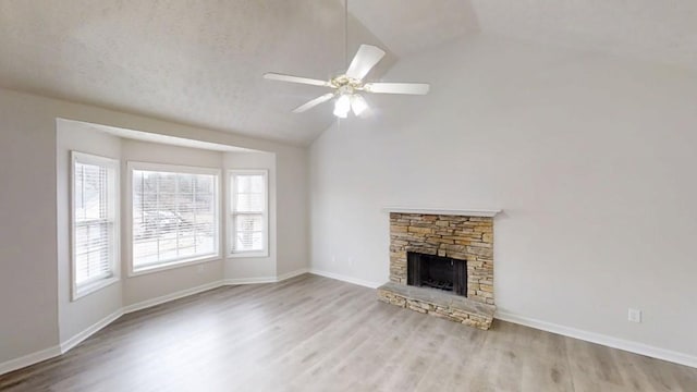 unfurnished living room featuring baseboards, vaulted ceiling, wood finished floors, and a stone fireplace