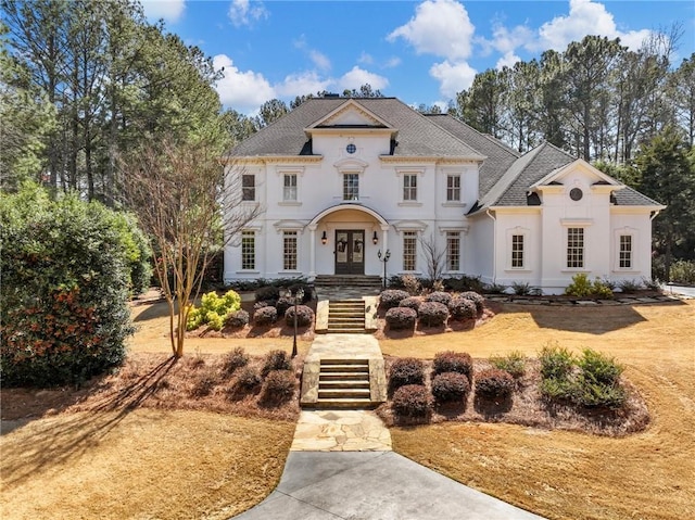 view of front facade with stucco siding, french doors, stairs, and roof with shingles