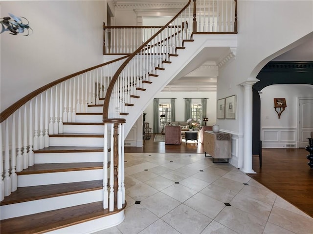 stairway with arched walkways, wainscoting, a decorative wall, decorative columns, and a towering ceiling