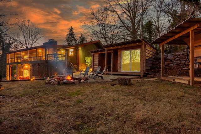 back house at dusk with a lawn, a fire pit, a sunroom, and a patio area