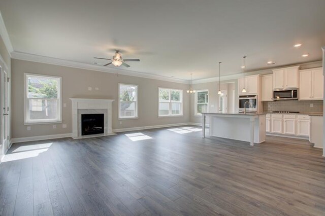 kitchen featuring a kitchen island with sink, stainless steel appliances, light stone countertops, white cabinets, and pendant lighting