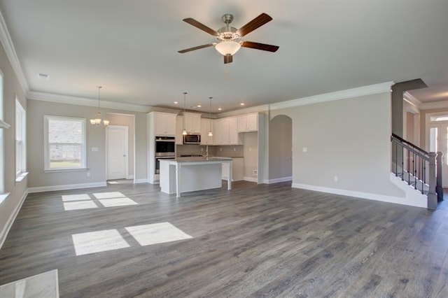 unfurnished living room with ceiling fan with notable chandelier, crown molding, and wood-type flooring