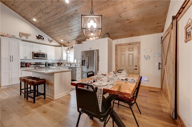 dining space with lofted ceiling, sink, light wood-type flooring, wooden ceiling, and a barn door