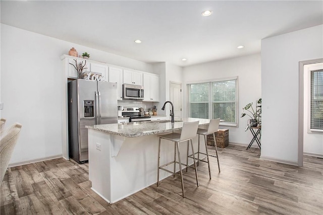 kitchen featuring stainless steel appliances, a sink, a kitchen island with sink, and light wood-style floors