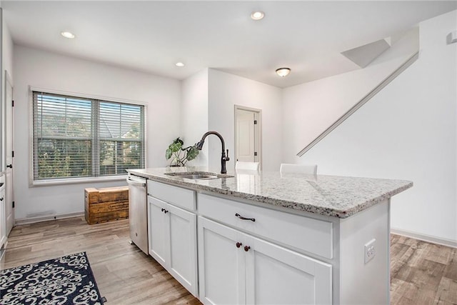 kitchen featuring light wood-type flooring, light stone countertops, white cabinetry, and a sink