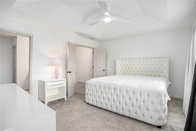 bedroom featuring baseboards, a tray ceiling, a ceiling fan, and light colored carpet