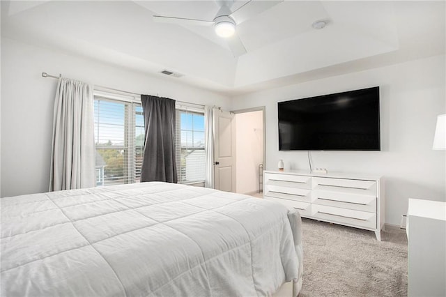 bedroom featuring light carpet, a ceiling fan, visible vents, and a tray ceiling