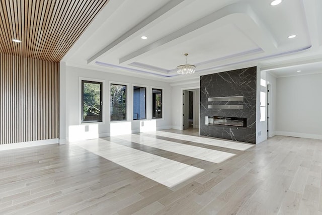 unfurnished living room with a raised ceiling, a premium fireplace, light hardwood / wood-style flooring, a chandelier, and ornamental molding