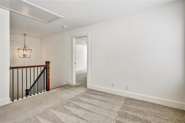 carpeted spare room featuring attic access, baseboards, and an inviting chandelier