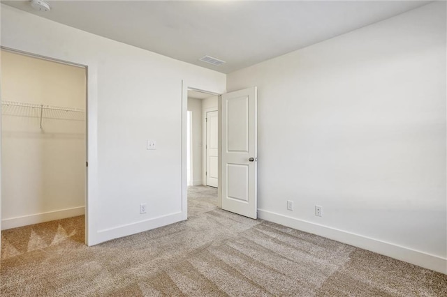 unfurnished bedroom with carpet floors, a walk in closet, a closet, visible vents, and baseboards