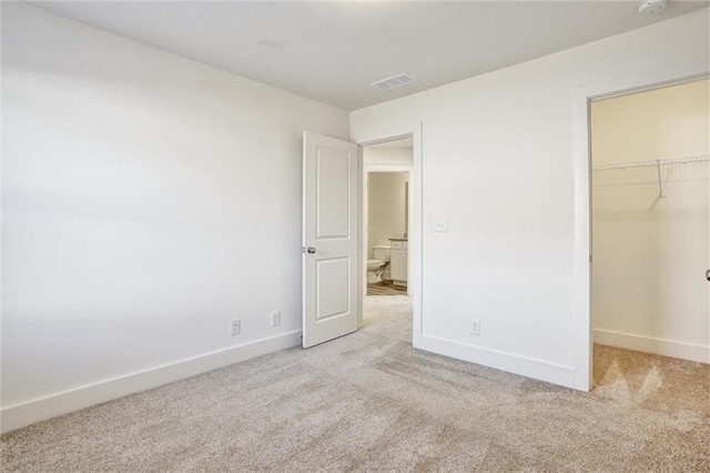 unfurnished bedroom featuring baseboards, a spacious closet, visible vents, and light colored carpet