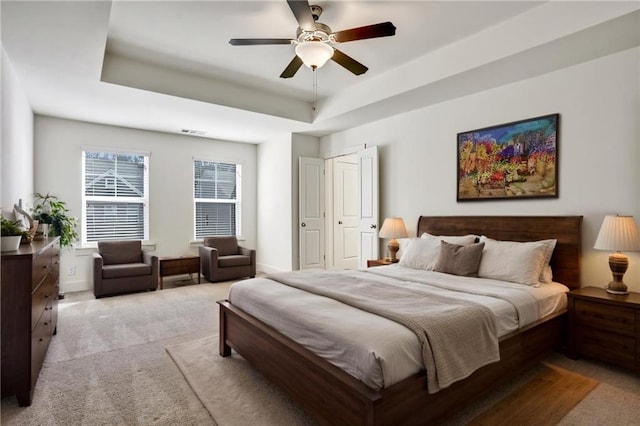 bedroom featuring visible vents, a tray ceiling, a ceiling fan, and light colored carpet