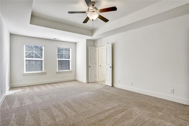 empty room with baseboards, a tray ceiling, visible vents, and light colored carpet