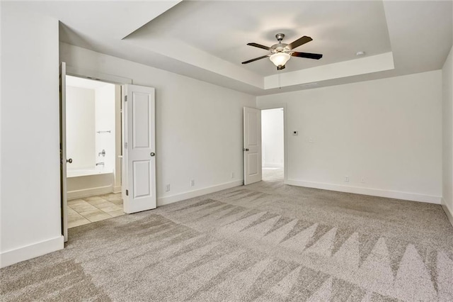 unfurnished bedroom featuring carpet floors, a tray ceiling, and baseboards