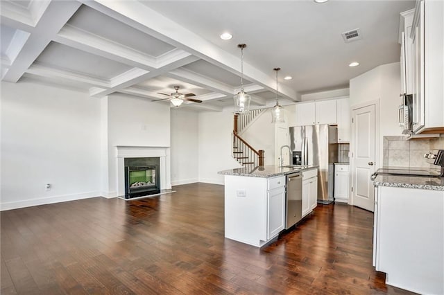 kitchen with visible vents, appliances with stainless steel finishes, a high end fireplace, dark wood-type flooring, and light stone countertops