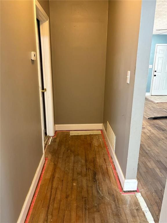 corridor with hardwood / wood-style flooring, visible vents, and baseboards