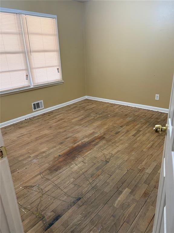 spare room with dark wood-type flooring, visible vents, and baseboards