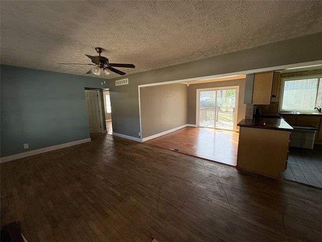 unfurnished living room featuring baseboards, visible vents, dark wood-style floors, ceiling fan, and a textured ceiling