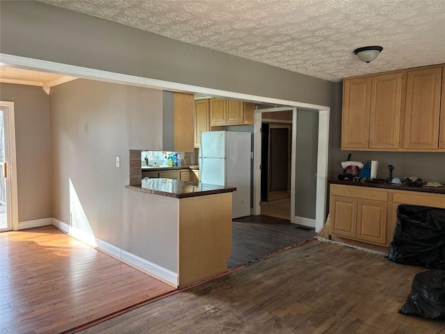 kitchen with dark countertops, wood-type flooring, baseboards, and freestanding refrigerator