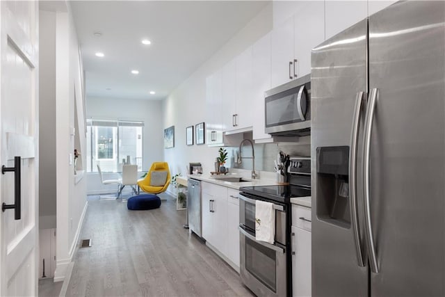kitchen with appliances with stainless steel finishes, a sink, light countertops, light wood-style flooring, and white cabinetry