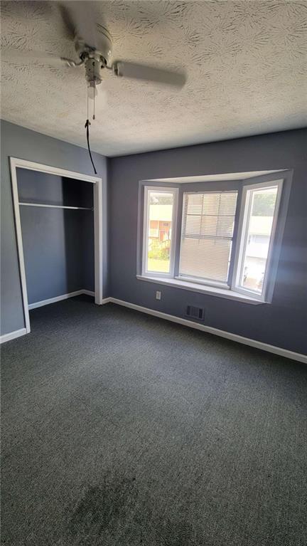 unfurnished bedroom with multiple windows, dark colored carpet, and ceiling fan