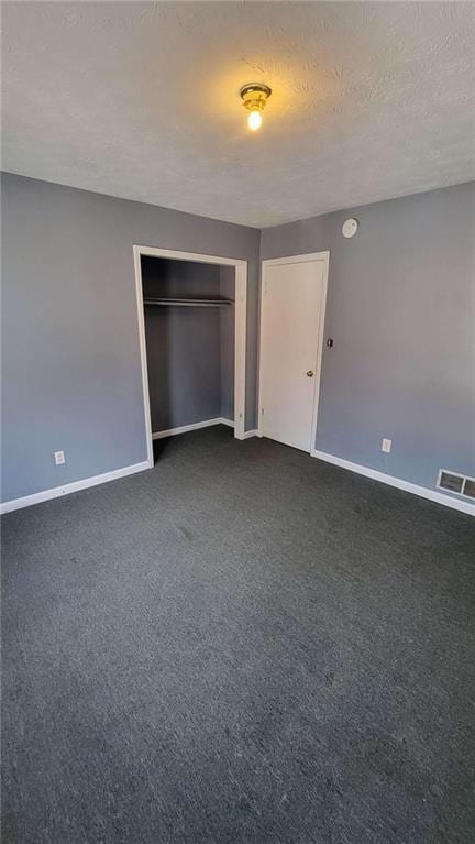 unfurnished bedroom with a textured ceiling, a closet, and dark colored carpet