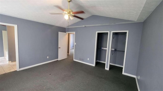 unfurnished bedroom featuring dark colored carpet, a textured ceiling, vaulted ceiling, multiple closets, and ceiling fan