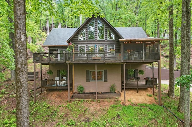 rear view of house with a garden, a deck, a sunroom, a view of trees, and stucco siding