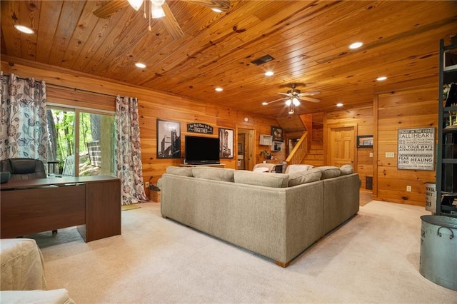 living room featuring wooden walls, ceiling fan, light colored carpet, stairs, and wooden ceiling