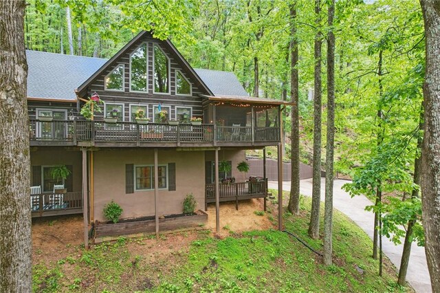 back of property featuring a wooden deck, stucco siding, a sunroom, driveway, and a wooded view