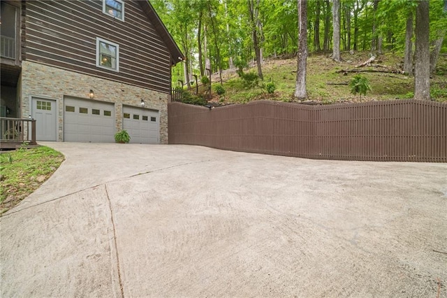 view of home's exterior with concrete driveway, an attached garage, fence, and stone siding