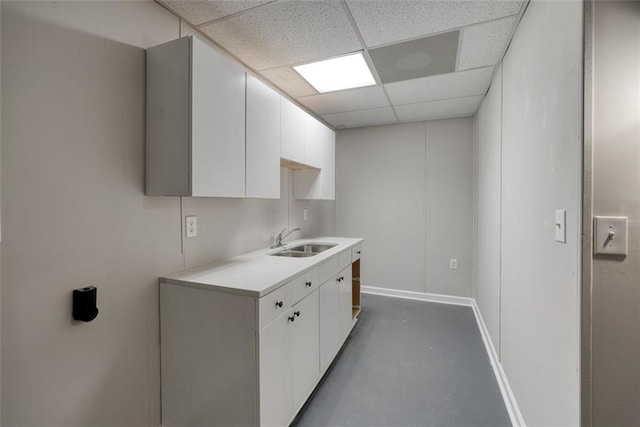 kitchen with a paneled ceiling, white cabinetry, sink, and concrete floors